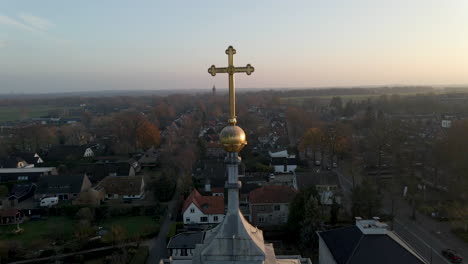 foque de crucifijo dorado en la torre de la iglesia con un pequeño pueblo rural en el fondo