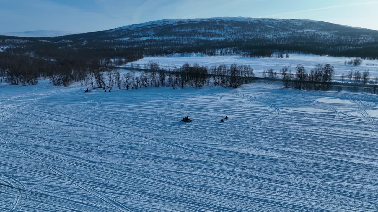 Beautiful aerial video of unrecognizable people on snowmobiles pull unrecognizable children on small snow sledges. Sunny winter day in Swedish Mountains. Joesjo, Sweden