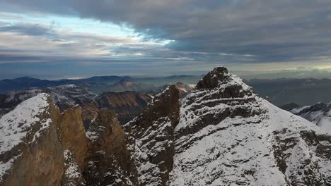 drone shot flying over the mountain tops of a bare, cold and snow covered mountain in the remote and secluded nature of switzerland