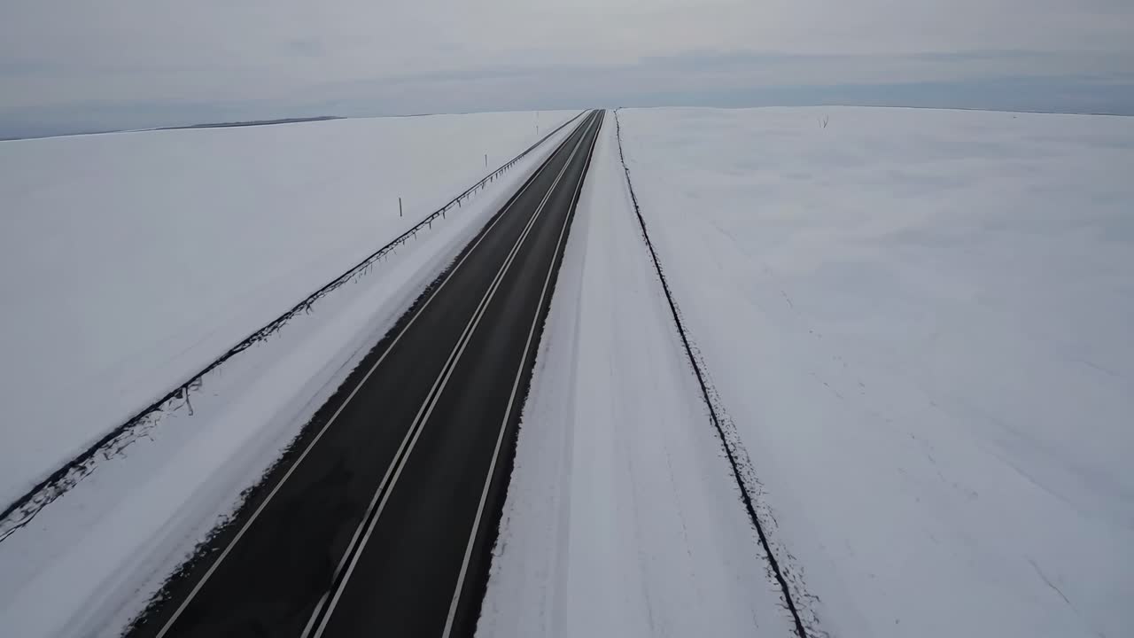 Aerial video captures a straight road cutting through a vast snowy landscape, emphasizing isolation