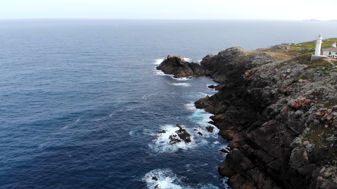 Vista aerea di un faro bianco su una scogliera frastagliata che si affaccia sull'oceano