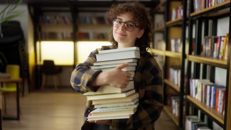 Portrait-of-a-girl-student-with-curly-hair-in-a-checkered-shirt-who-holds-a-stack-of-papers-in-her-hands-near-the-shelves-in-the-library