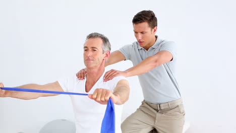 physiotherapist checking senior patient stretching blue resistance band