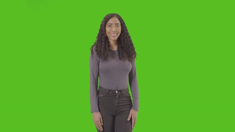 three quarter length studio portrait of woman against green screen smiling at camera