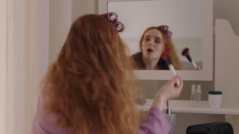 Schönes-Teenager-Mädchen-Mit-Roten-Haaren,-Das-Sich-Fertig-Macht-Und-In-Den-Spiegel-Schaut,-Make-up-Aufträgt-Und-Das-Ausgehen-Am-Wochenendmorgen-Vorbereitet