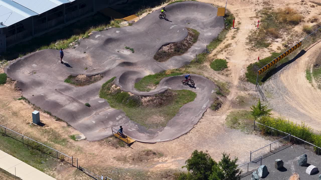 Foto aérea de um drone em um ângulo alto de ciclistas de montanha percorrendo uma pista de asfalto curva sob a luz do dia