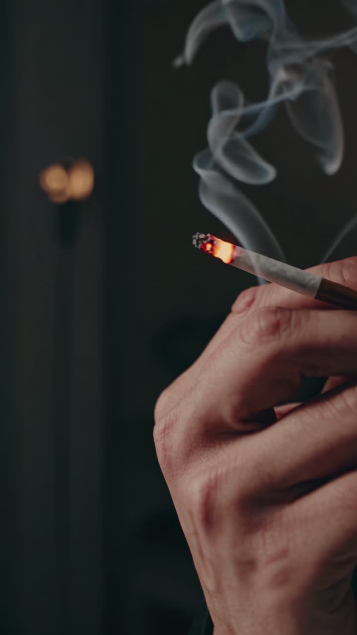 Close-up shot of a hand holding a lit cigarette, smoke swirling upwards