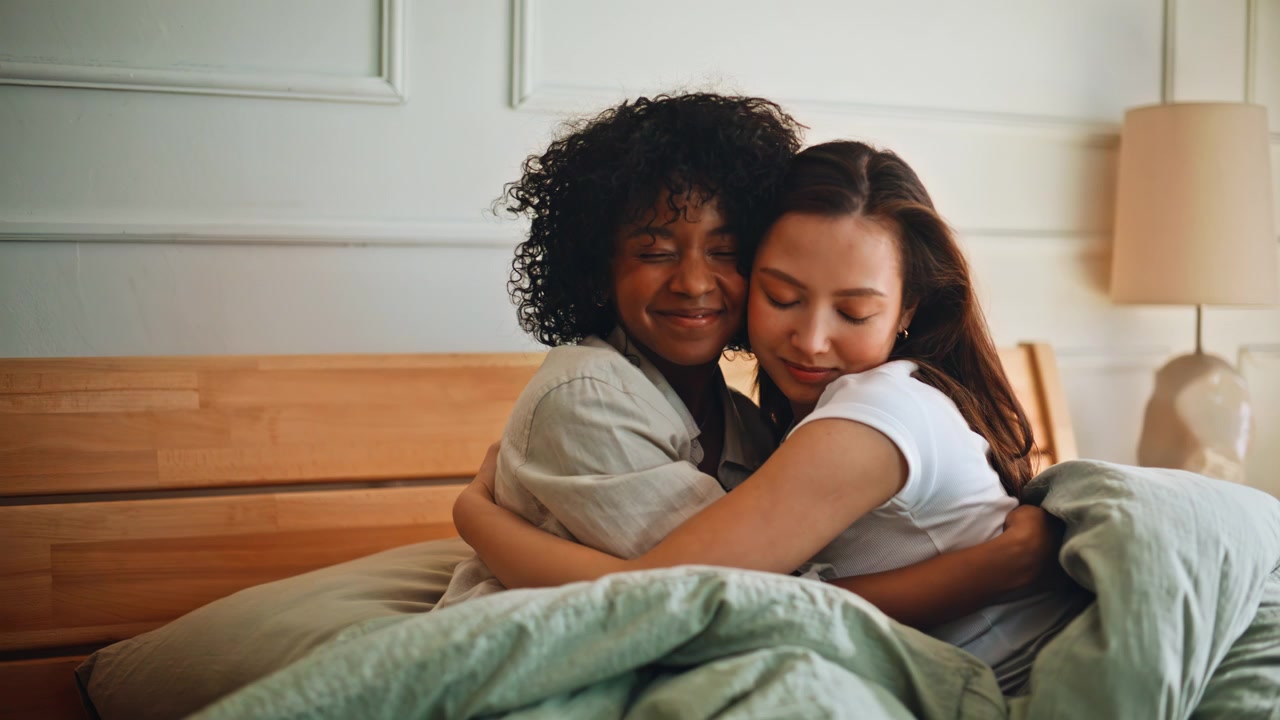 Coppia lesbica che si abbraccia a letto. Partner interrazziali che si stringono teneramente a casa al mattino.