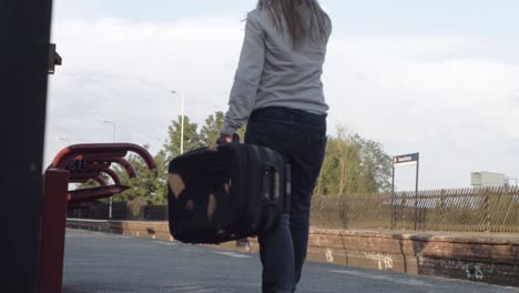 Woman-picks-up-suitcase-on-train-platform-medium-shot