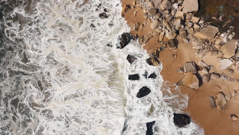 Aeriao-circle-shot-of-water-waves-arriving-sandy-and-rocky-beach-of-Nazare