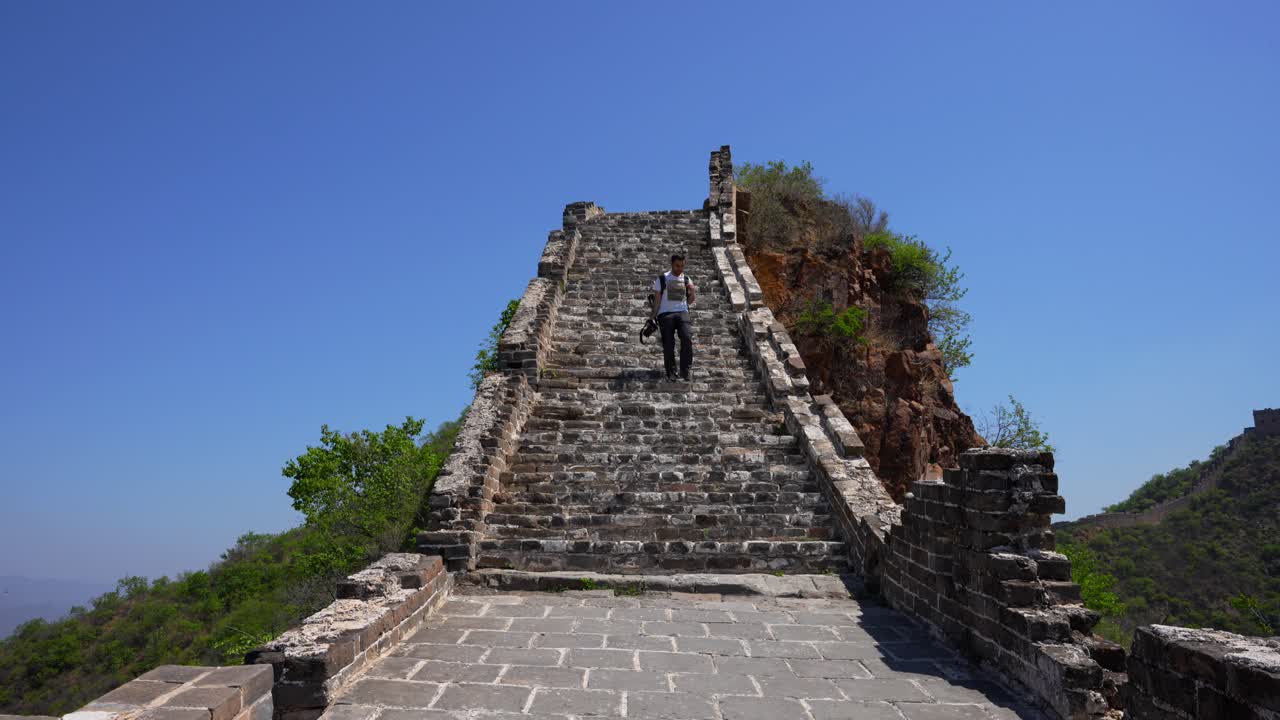 Man descends steps in the Great Wall’s Jinshanling section, surrounded by nature on a sunny day