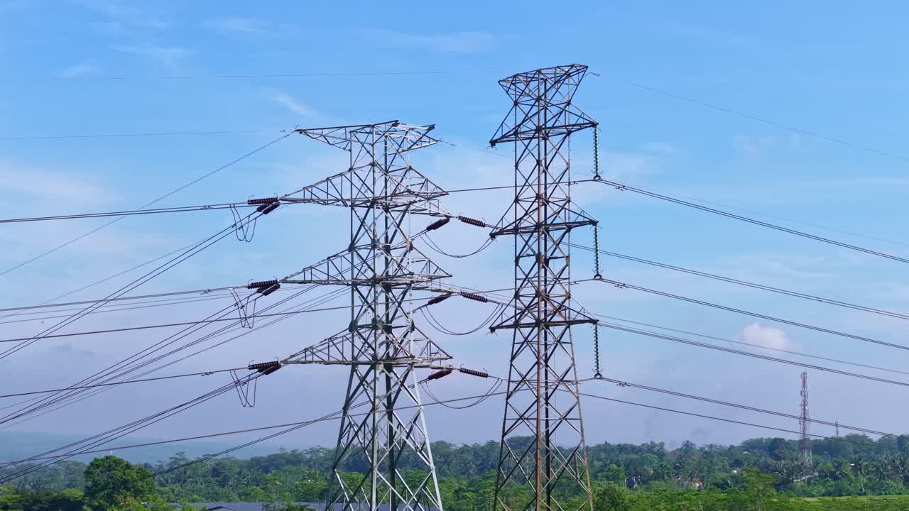 High voltage power transmission towers standing across green landscape under blue sky, showcasing energy infrastructure and electricity distribution network in rural area