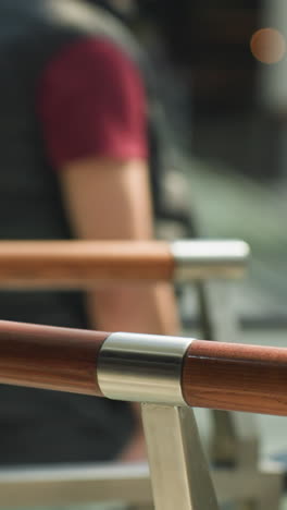 a bustling mall scene captured from a first-person perspective with a handheld camera, featuring a blurred background. the focus is on sleek wooden handrails with a person holding onto them