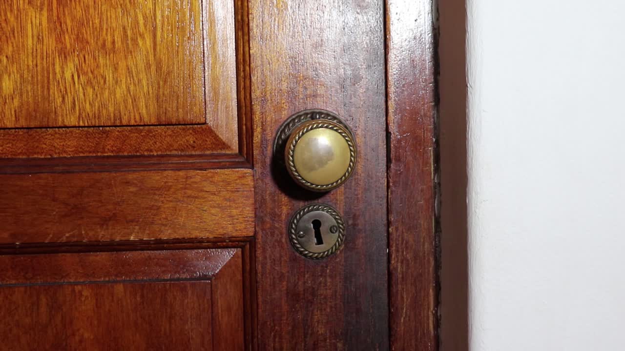 Brass Door knob turns and man with black glove opening wooden door slowly