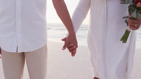 las manos de una pareja recién casada en la playa al atardecer.