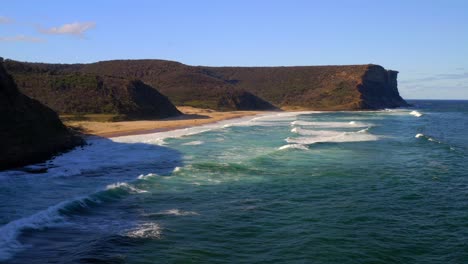 Olas-Marinas-En-La-Orilla-De-La-Playa-De-Garie-Con-Vistas-A-La-Cabeza-Norte-De-Garie-En-El-Parque-Nacional-Real,-Nsw,-Australia---Toma-Aérea-De-Drones