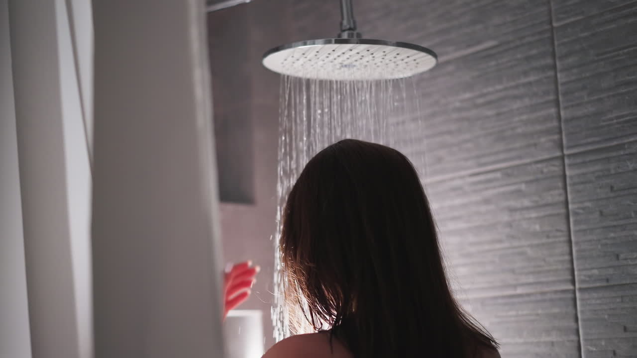 mujer se encuentra bajo sprays de ducha en el baño de cerca. dama se relaja en la caída de gotas de agua en el baño del hogar. equipo de lavado del cuerpo en el apartamento