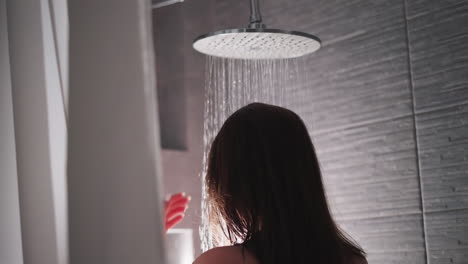mujer se encuentra bajo sprays de ducha en el baño de cerca. dama se relaja en la caída de gotas de agua en el baño del hogar. equipo de lavado del cuerpo en el apartamento