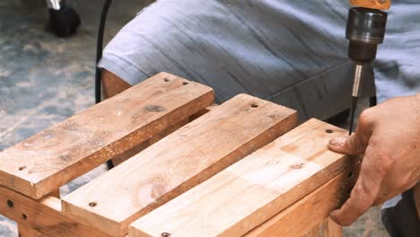 skillfull carpenter employing a power drill to attaching screws into a small wooden chair in his small business workshop to sell and support the local economy