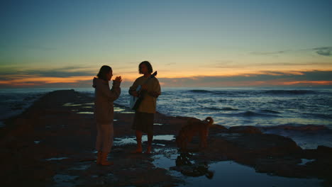 pair silhouettes dating sunset beach. woman enjoying music man playing guitar