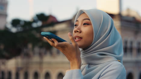 young muslim woman using smartphone voice assistant outdoors