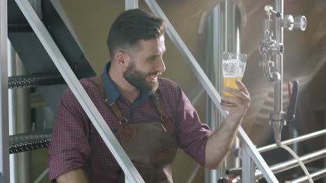 young brewer wearing a leather apron is tasting beer at a modern brewery