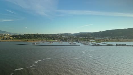 aerial pan across harbor entrance and wetlands along carquinez strait regional shoreline in martinez, california as sunlight glistens on water