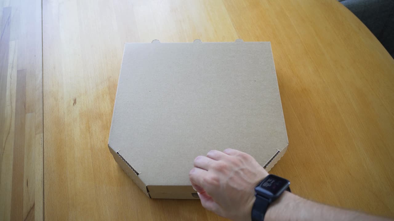 the handheld shot of man's hand opening delivered Italian pizza in a cardboard box on the table at home