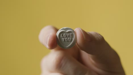 gros plan sur une main tenant des bonbons au coeur avec un message d'amour sur fond jaune