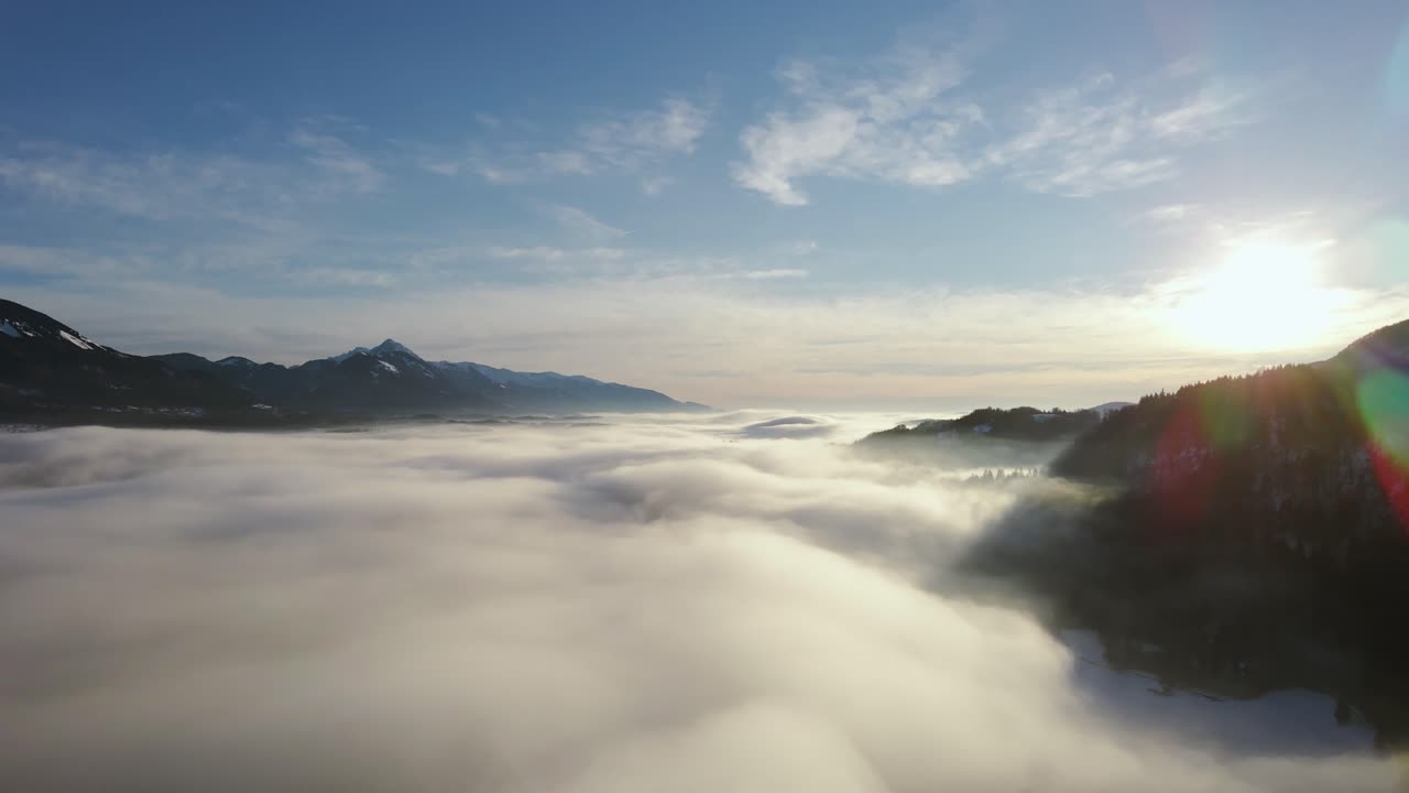 Drone shot  of an incredible landscape covered under the fog with surrounding mountains in the morning at winter time in Slovenia captured in 4k, drone going down under the fog