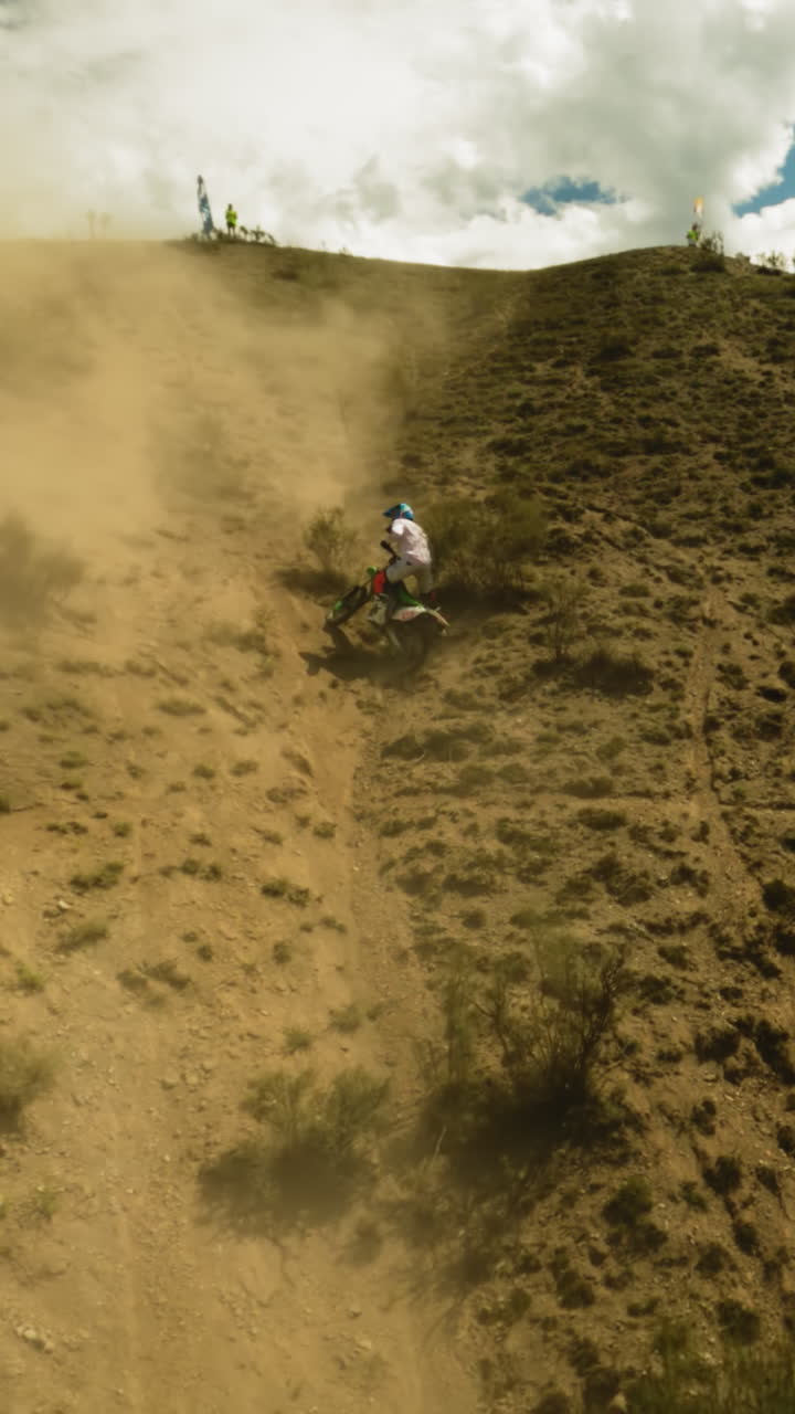 el motociclista se mueve cuesta abajo resbalando en el polvo del dron fpv. el deportista se ocupa de los problemas de la motocicleta durante las carreras en las tierras altas del desierto.