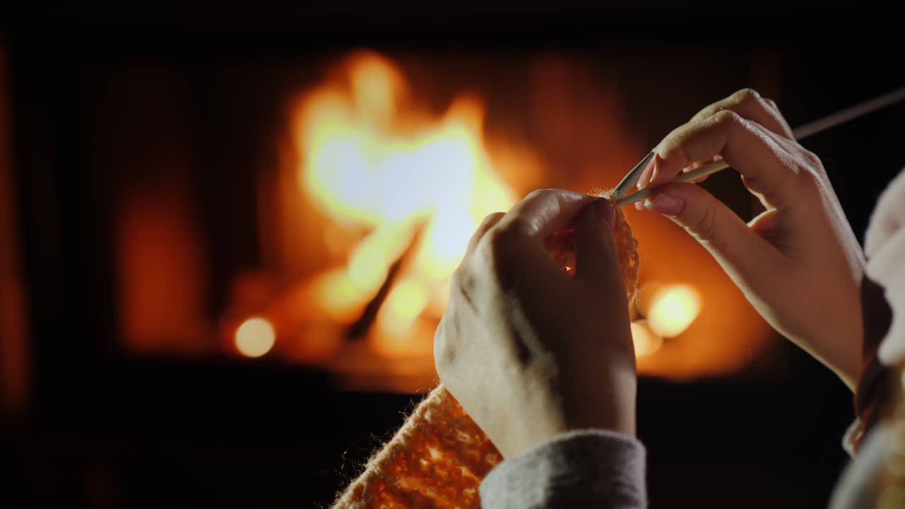 manos femeninas con agujas de tejer - teje ropa de abrigo sentada junto a la chimenea