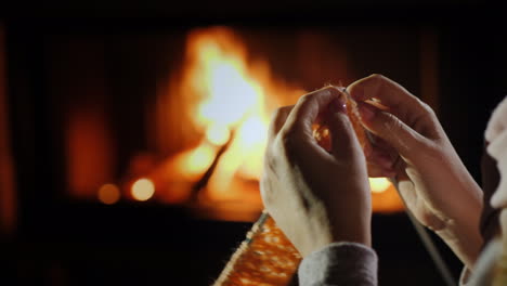 female hands with knitting needles - knits warm clothes sitting by the fireplace