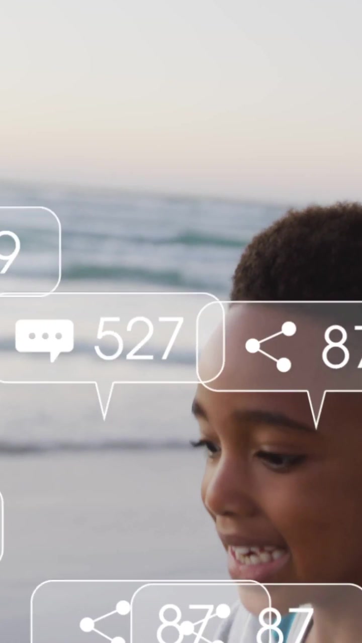 Vertical video: Boy prompted by social alerts moving right dusk shore as icons popping and clumping