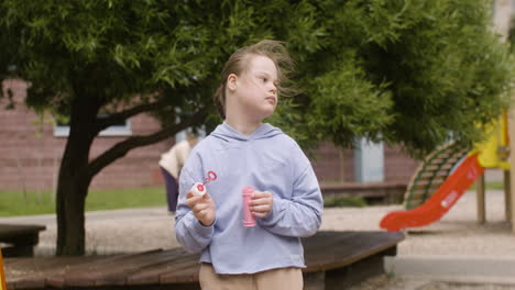 little girl with down syndrome blowing soap bubbles in the park on a windy day