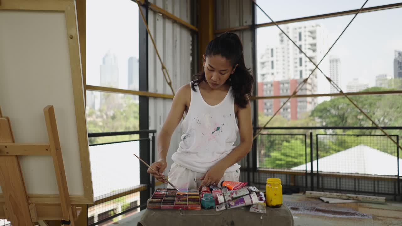 A woman artist painting in her studio with a city view