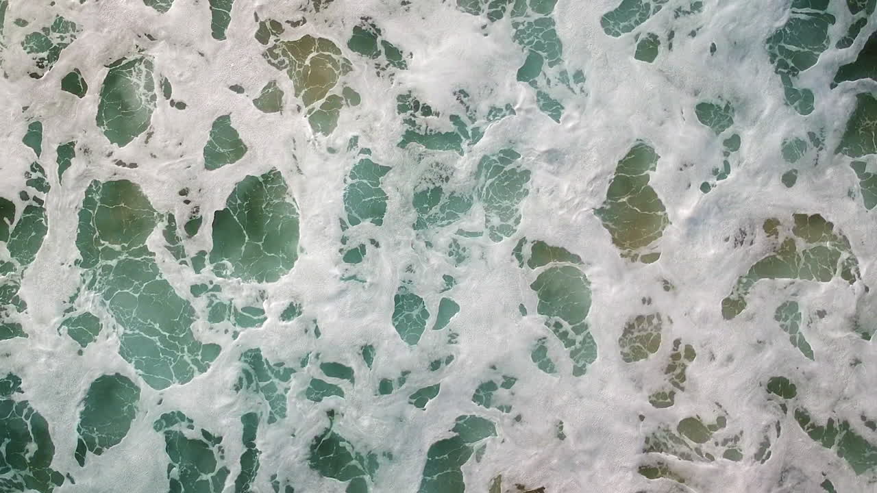 toma aérea de drones de olas de aguas bravas rodando en una playa en algarve, portugal