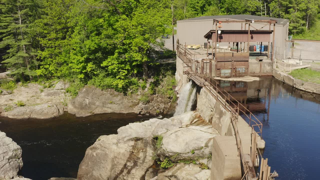 Aerial view of river water flowing through an hydro electric dam, surrounded by forest trees