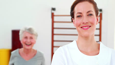 terapeuta físico sonriendo a la cámara con el paciente bailando en el fondo