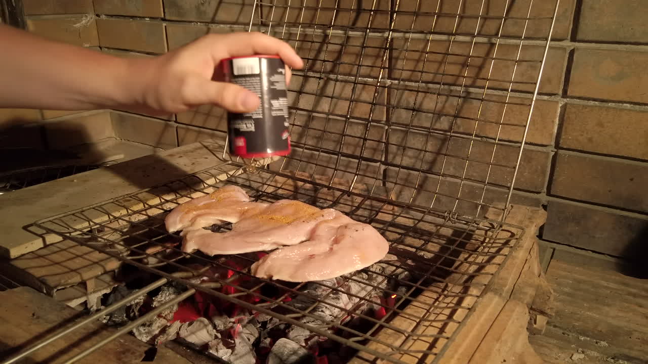 밤에 숯불 바베큐에 구운 닭고기에 조미료를 추가하는 남자의 핸드헬드 샷