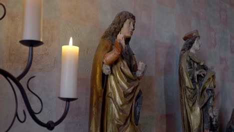 two religious figurines standing in the hall of a historic castle, viewed through candles