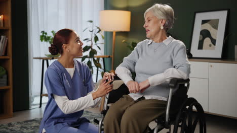 elderly woman in wheelchair talking to caretaker at home