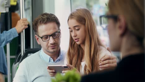 Close-Up-Of-The-Good-Looking-Man-In-Glasses-Going-In-The-Tram-With-His-Pretty-Cute-Teenage-Daughter-While-She-Showing-Him-Something-On-The-Smartphone