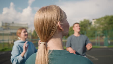 back view of lady in green hoodie with hair tied, training volleyball with teammates in background, focused on teamwork and volleyball practice in an outdoor setting