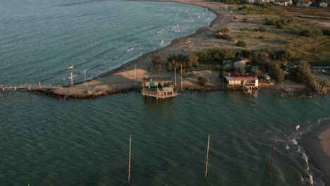 Aerial-shot-of-the-valleys-near-Ravenna-where-the-river-flows-into-the-sea-with-the-typical-fishermen's-huts-at-sunset