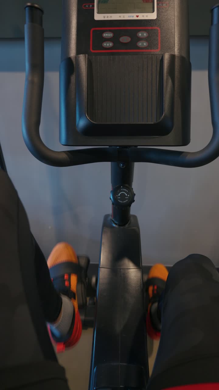 Overhead close-up of a person wearing black leggings and orange shoes pedaling on a spin bike during a cardio workout at an indoor fitness studio - vertical