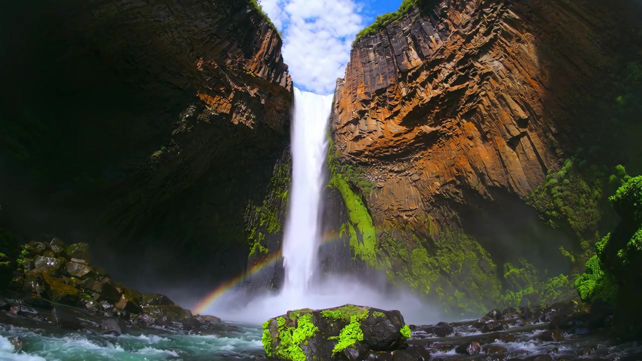 Potente cascata e arcobaleno in una gola rocciosa e verdeggiante