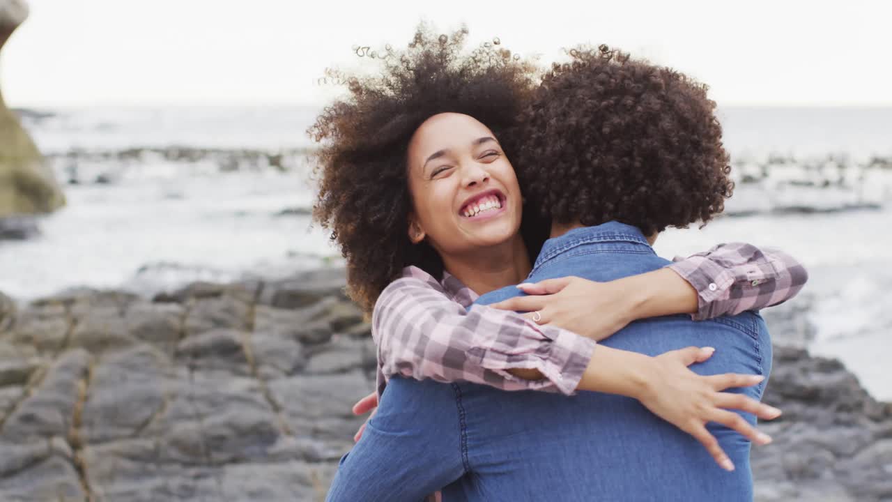mujer afroamericana abrazando a su marido en las rocas cerca del mar