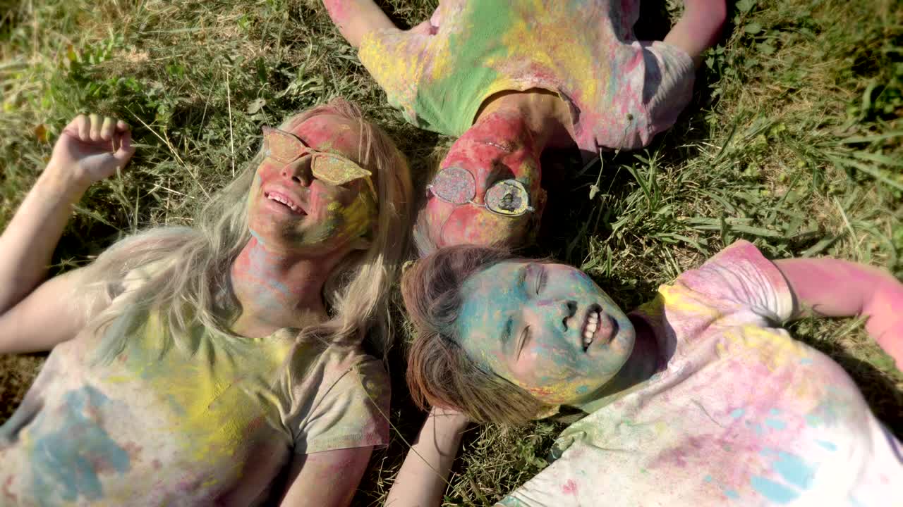 Three young happy multi-ethnic girlfriends are laying on grass on holi festival in daytime in summer, friendship concept, holiday concept
