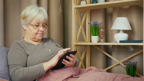 Older-woman-relaxes-in-her-room-and-uses-a-tablet-1